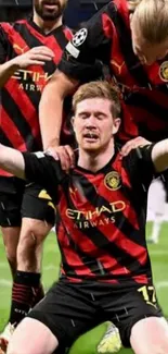 Soccer players celebrating in black and red jerseys on the field.