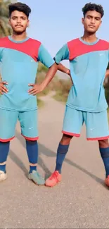 Two young athletes in blue-red soccer kits posing confidently on a path.