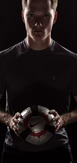 Soccer player holding a ball on a dark background.