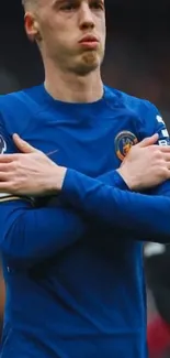 Soccer player celebrates in vibrant blue jersey with crossed arms.