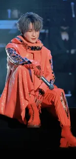 Energetic stage performer in orange outfit on stage under bright lights.