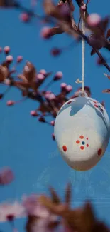 Easter egg decoration hanging among spring blossoms with blue sky backdrop.