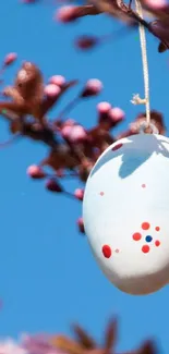 Easter egg hanging on a blooming branch with sky background.