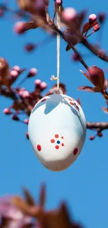 Easter egg hanging on a spring branch with blue sky background.