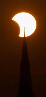 Solar eclipse above a church spire at sunset.