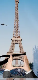 Eiffel Tower framed with hands and airplane in sky.