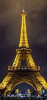 Illuminated Eiffel Tower at night with cloudy sky.