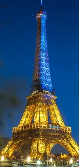 Eiffel Tower lit at night with reflections on the Seine against a royal blue sky.