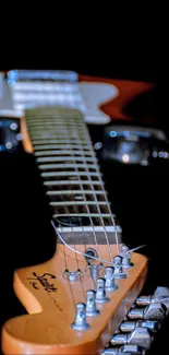 Close-up of an electric guitar neck with strings against a black background.