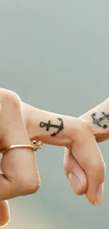 Intertwined fingers with anchor tattoos on light gray background.