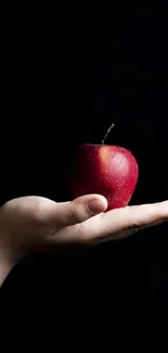 Minimalist wallpaper of a hand holding a red apple against a black background.