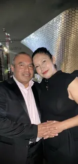 Couple posing against a modern architectural backdrop at night.