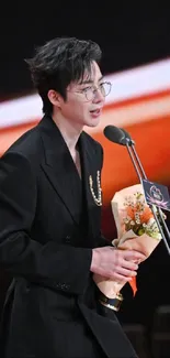 Person in black suit with bouquet at ceremony stage.