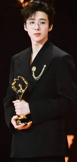 Person in a black suit holding a golden trophy at an award event.