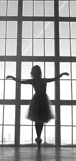 Silhouette of a ballerina posing gracefully against a large window.