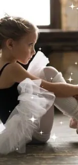 Young ballerina in tutu seated gracefully on a wooden floor.