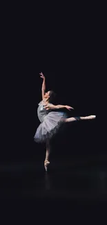 Ballet dancer posing elegantly on stage against a dark background.