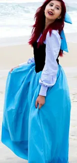 Woman in blue dress at beach, standing gracefully by the ocean.