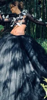 Elegant woman in a black gown posing in a lush garden setting.