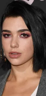 Portrait of a woman with black hair and striking makeup on a dark background.