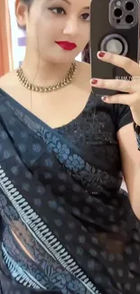 Woman in elegant black saree with smartphone.