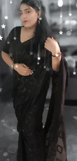 Woman in a black saree standing in a room, exuding elegance.