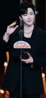 Stylish person in a black suit holding an award with warm glowing lights.