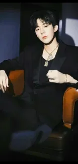 Person in a stylish black suit sitting elegantly on a chair.