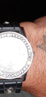 Close-up of a black watch on tattooed wrist.