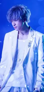 Artist in white suit on stage with blue background.