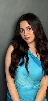 Woman in elegant blue dress against dark background.