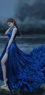 Model in a flowing blue dress by a serene lake landscape.