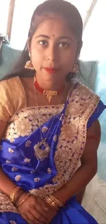 Woman in blue saree sitting indoors, showcasing elegance and tradition.