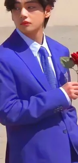 Person in blue suit with red rose, standing elegantly.