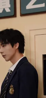 Stylish young man in school uniform posing thoughtfully against a beige wall.