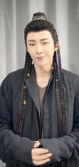 Person with braided hair in a traditional outfit against a gray background.