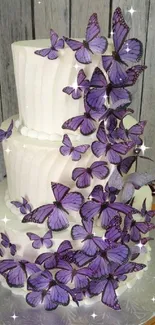 Three-tier white cake with purple butterflies on rustic background.