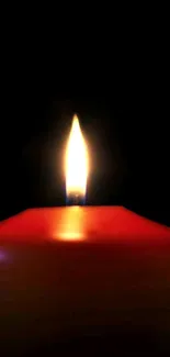 A glowing candle flame with a red wax on a dark background.