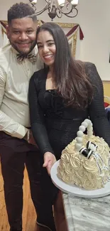 A smiling couple poses with a decorative cake indoors, capturing a festive moment.