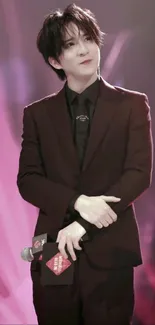 Elegant celebrity wearing a black suit on stage, surrounded by burgundy hues.