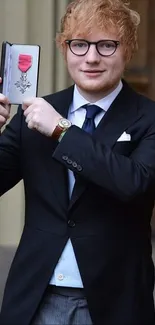 Man displaying an award medal in formal attire.