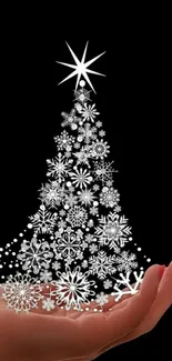 Hand holding snowflake Christmas tree on black background wallpaper.