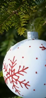 White ornament with red snowflakes on pine tree background.