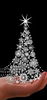 Hand holding a shimmering silver Christmas tree on a black background wallpaper.