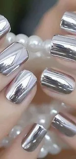 Close-up of chrome manicured nails holding a white pearl bracelet.