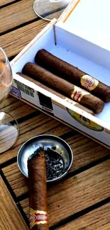 Cigars on a wooden table with whiskey and ashtray.