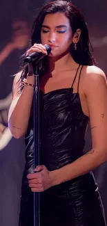 Singer in black dress on stage, holding a microphone.