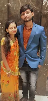 Couple in vibrant attire with a marble backdrop.