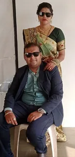 Elegant couple seated in sunglasses, full view.