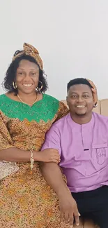 Couple in vibrant traditional attire seated on a sofa, showcasing cultural fashion.